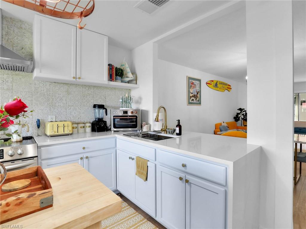 9831 Alabama Street, Unit 5 Bonita Springs, FL 34135 - Photo 8 of 28 Kitchen featuring a peninsula, wall chimney exhaust hood, tasteful backsplash, open shelves, and white cabinetry