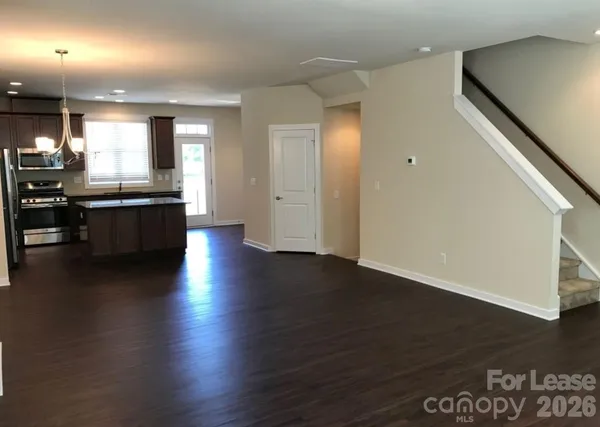 an empty room with wooden floor and kitchen view