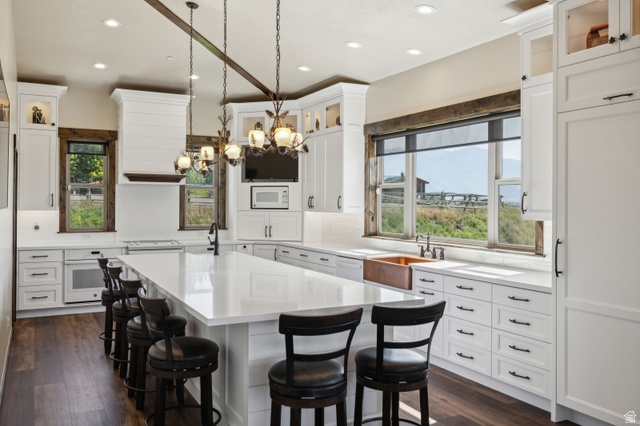 6117 North Rocky Ridge Road Peoa, UT 84061 - Photo 41 of 82 Spacious kitchen featuring an extended island with seating, white shaker cabinetry, wood-finish flooring, a farmhouse-style copper sink, and exposed ceiling beams