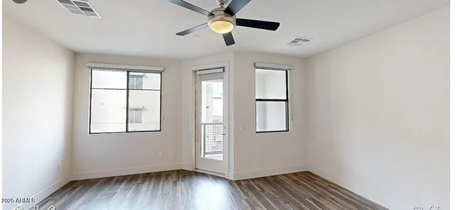 an empty room with wooden floor ceiling fan and windows