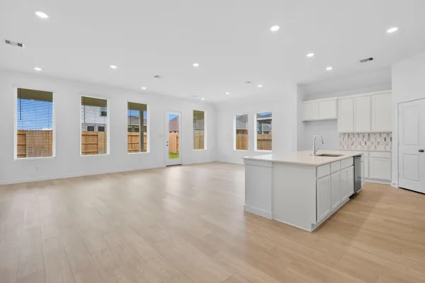 a large white kitchen with kitchen island a sink wooden floor and a refrigerator