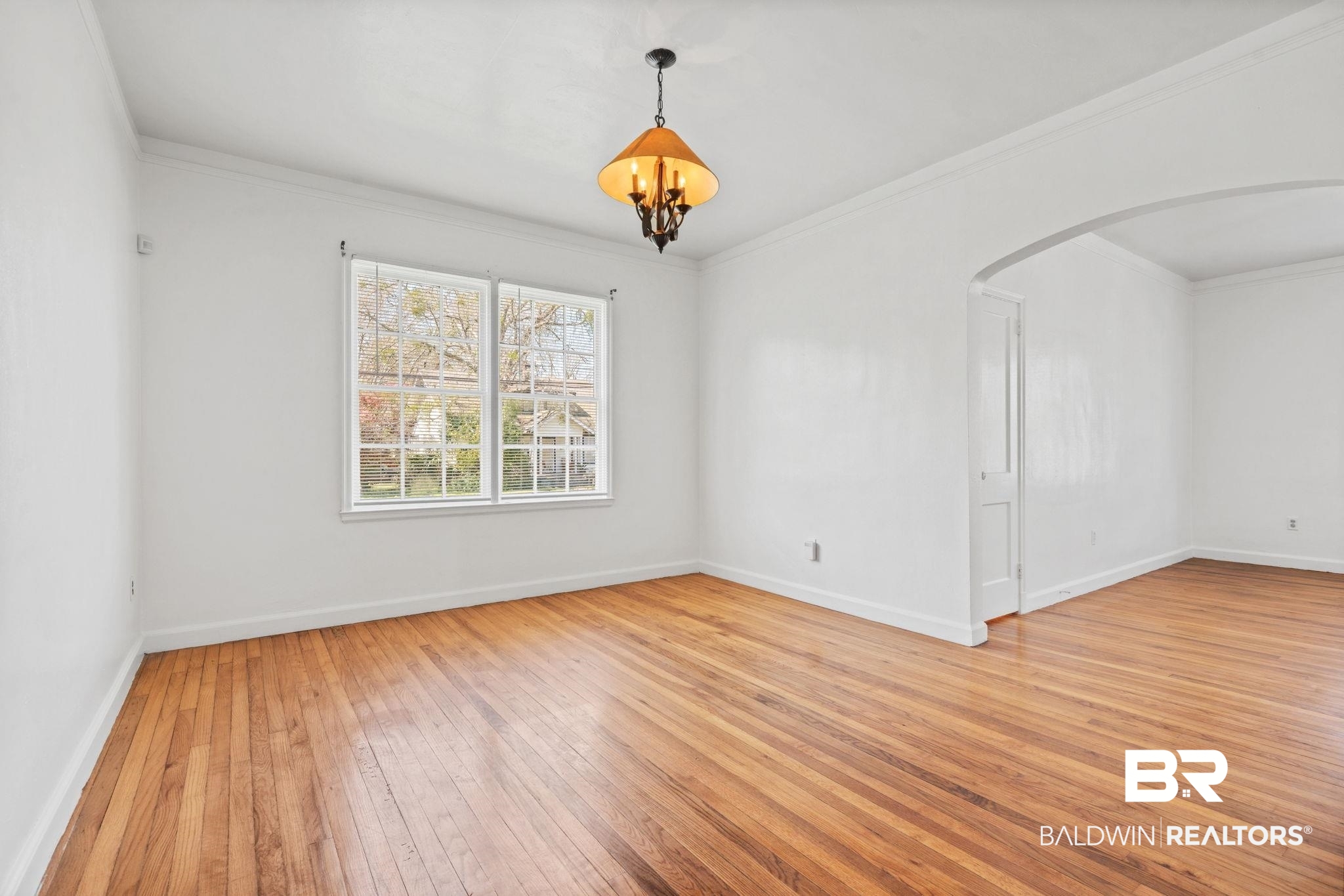 1707 Church Street Mobile, AL 36604 - Photo 11 of 43 Empty room with ornamental molding, arched walkways, light wood-style floors, baseboards, and a chandelier