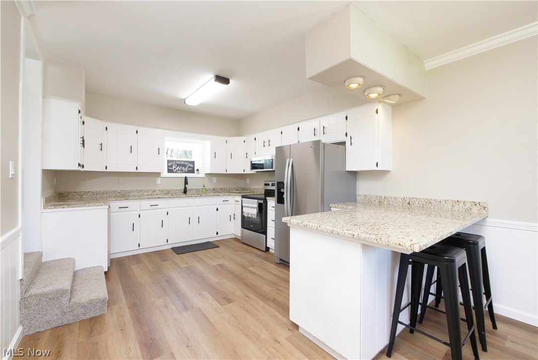 12379 Portage Street Rittman, OH 44270 - Photo 13 of 44 Kitchen with appliances with stainless steel finishes, light hardwood / wood-style floors, white cabinets, and light stone countertops