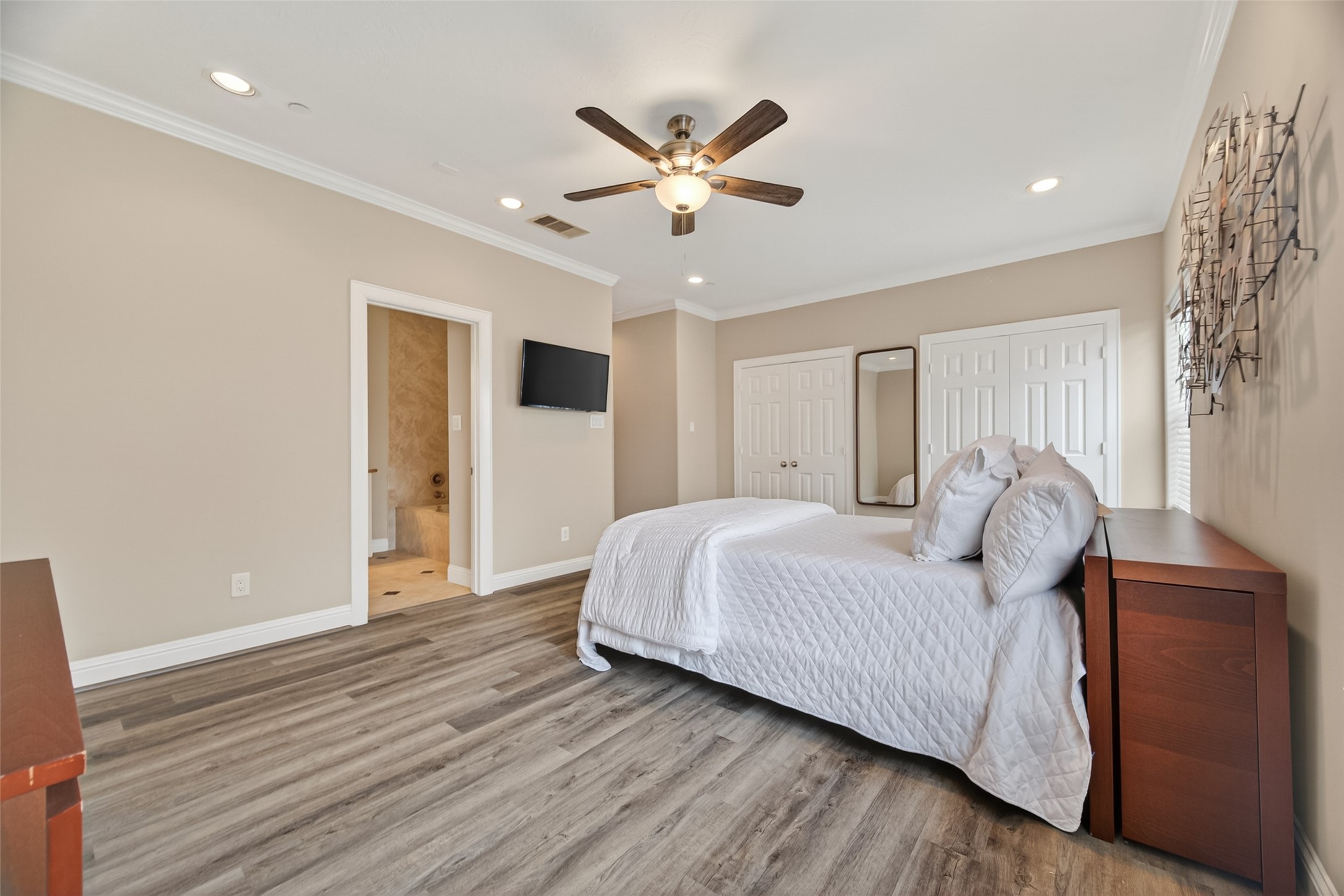 2611 Riverside Drive, Unit C Houston, TX 77004 - Photo 30 of 50 Spacious bedroom with wood flooring, neutral walls, and recessed lighting. Features a ceiling fan, wall-mounted TV, and large closet. Ensuite bathroom and ample natural light complete the inviting space.