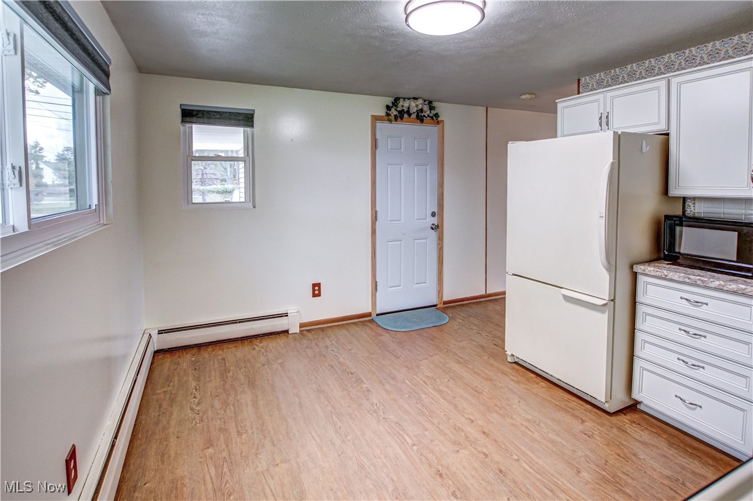 706 Abbe Road South Elyria, OH 44035 - Photo 11 of 34 Kitchen with light wood-style laminate flooring, freestanding refrigerator, white cabinets, a baseboard heating unit, and black microwave