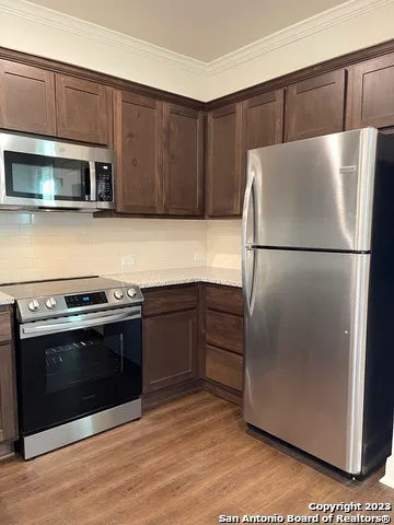 a white refrigerator freezer and a stove sitting inside of a kitchen with stainless steel appliances wooden floor