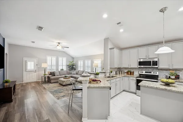 a open kitchen with stainless steel appliances granite countertop a stove top oven a sink a dining table and chairs with wooden floor