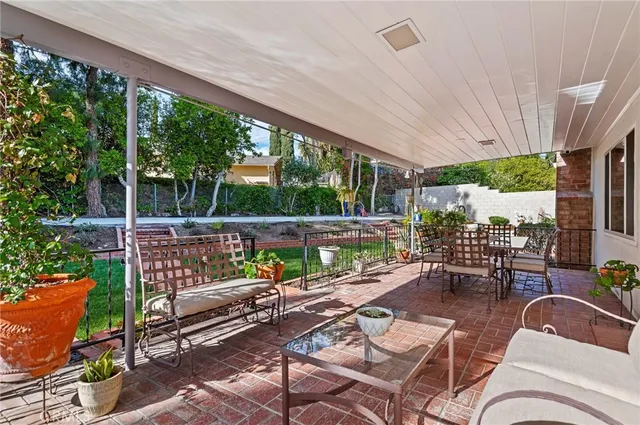 a view of a patio with couches chairs dining table and chairs barbeque grill with a small yard and large trees