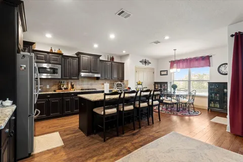 a kitchen with stainless steel appliances kitchen island granite countertop a table chairs and a refrigerator