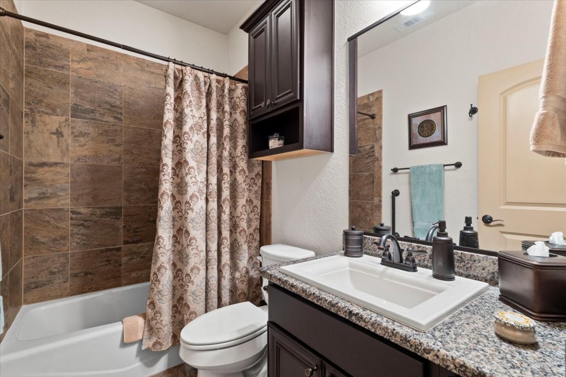 224 Whitney Woods Circle Georgetown, TX 78633 - Photo 25 of 40 a bathroom with a granite countertop sink toilet a mirror a bathtub and shower