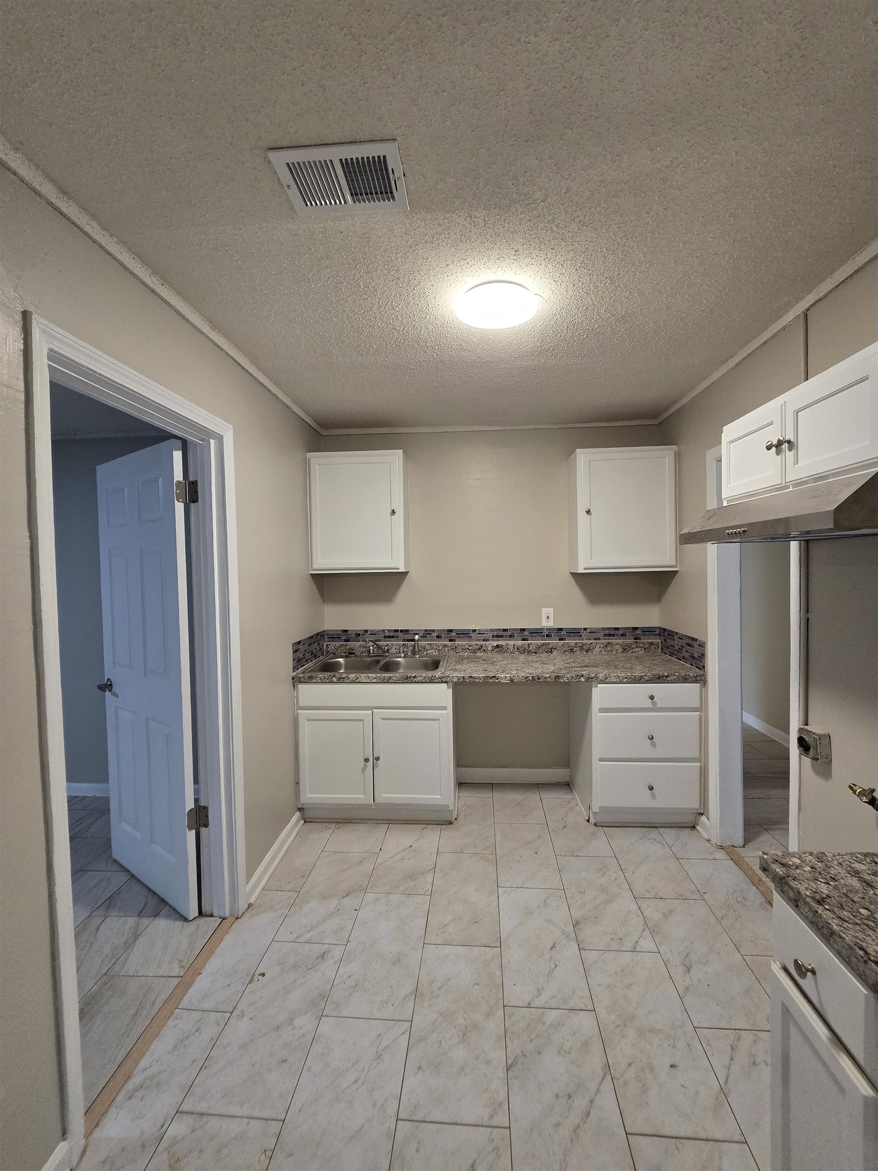 3198 Millwood Road Memphis, TN 38109 - Photo 2 of 5 Kitchen with a textured ceiling, white cabinets, dark stone counters, light marble finish floors, and ornamental molding