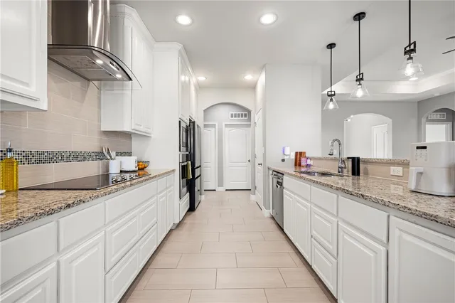 a large kitchen with granite countertop a large white cabinets and chandelier