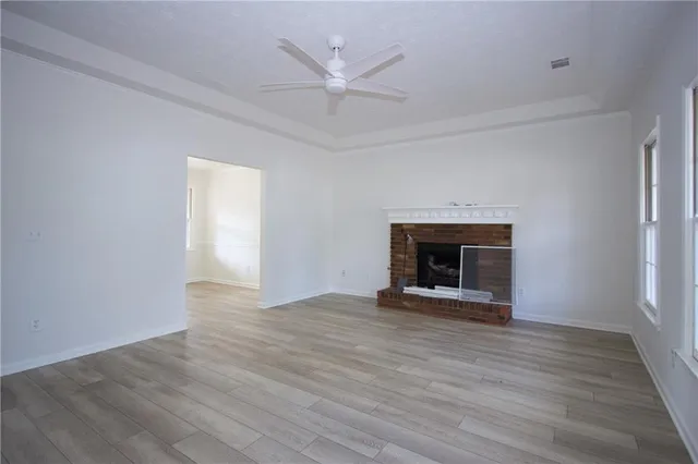 an empty room with wooden floor a fireplace and a ceiling fan