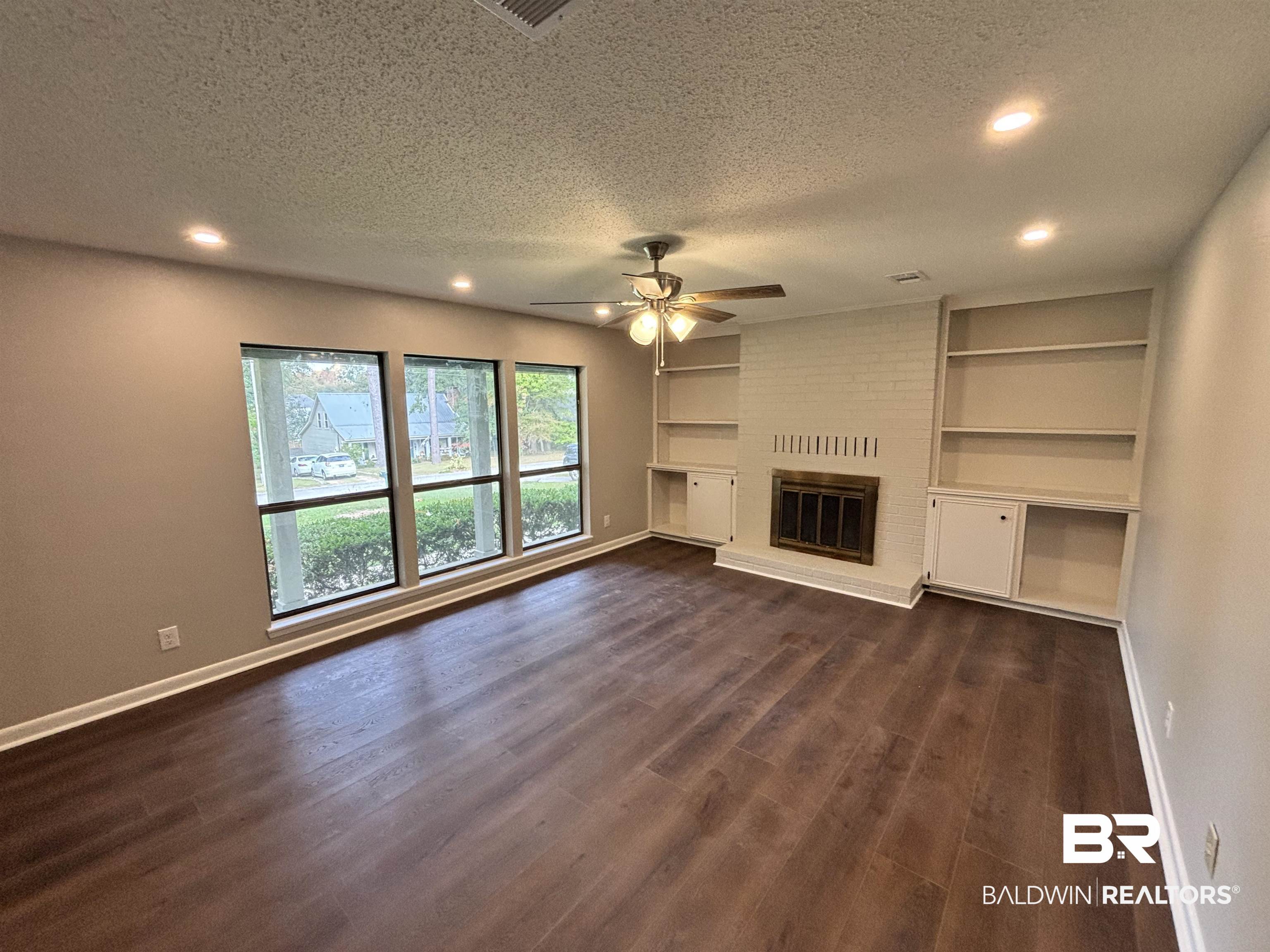 10 Soldiers Route Daphne, AL 36527 - Photo 6 of 26 Unfurnished living room featuring a textured ceiling, a brick fireplace, recessed lighting, built in features, and dark wood-type flooring