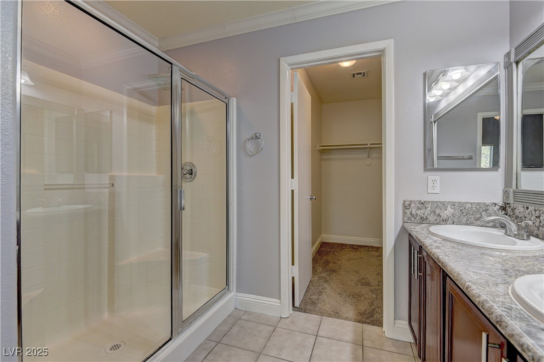 10654 Solar Hawk Avenue Las Vegas, NV 89129 - Photo 19 of 26 Full bath with light tile patterned floors, a shower stall, double vanity, a walk in closet, and ornamental molding