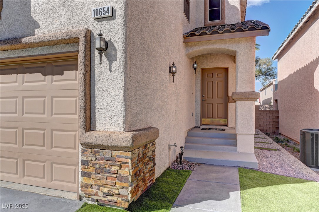 10654 Solar Hawk Avenue Las Vegas, NV 89129 - Photo 3 of 26 Doorway to property with stucco siding, a garage, and stone siding