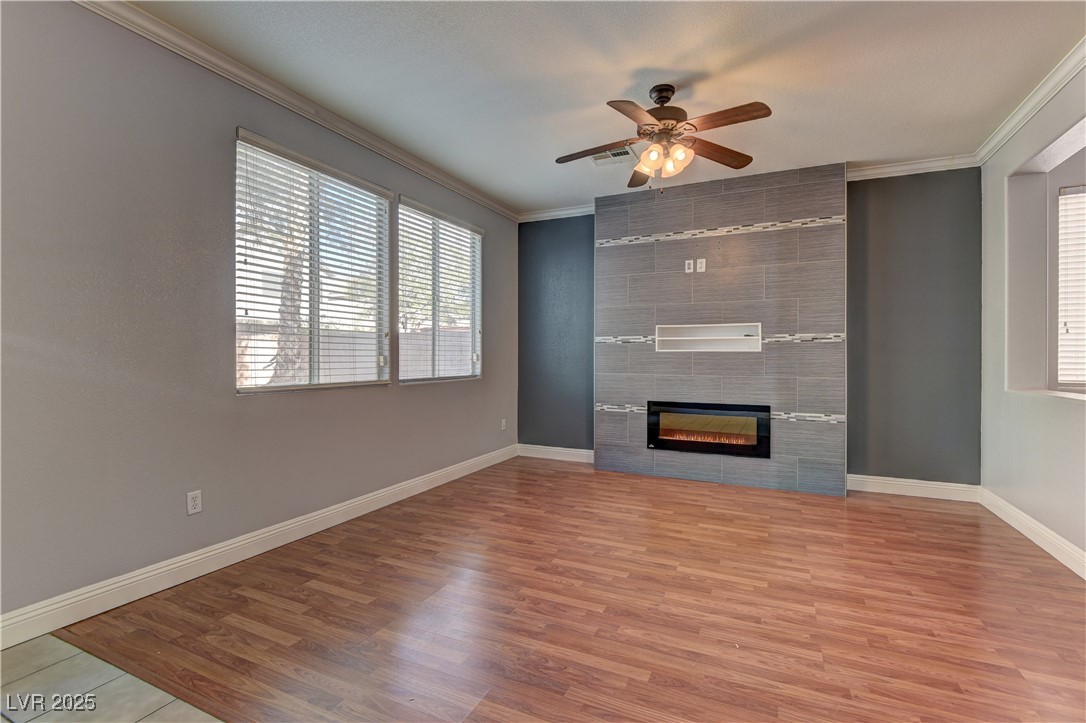 10654 Solar Hawk Avenue Las Vegas, NV 89129 - Photo 7 of 26 Unfurnished living room with ornamental molding, light wood-style flooring, ceiling fan, and a tiled fireplace