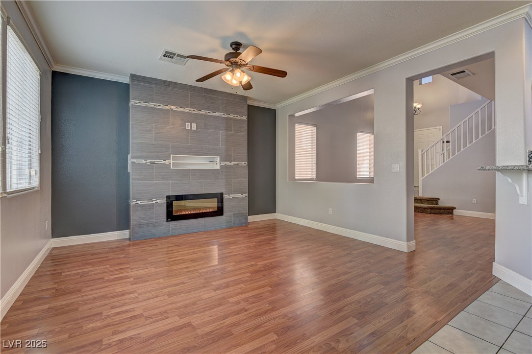 10654 Solar Hawk Avenue Las Vegas, NV 89129 - Photo 9 of 26 Unfurnished living room featuring crown molding, light wood-style flooring, stairs, a ceiling fan, and a tiled fireplace
