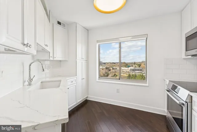 a kitchen with stainless steel appliances a sink a stove a refrigerator and white cabinets with wooden floor