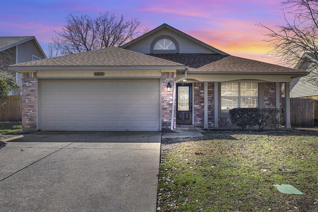 View of front facade with fence, a garage, brick siding, roof with shingles, and driveway