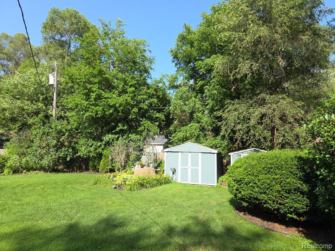 445 Clark Road Highland, MI 48357 - Photo 6 of 7 Expansive lawn with mature trees, established garden beds, and two storage sheds