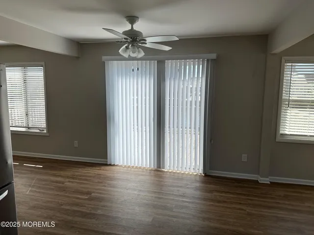 an empty room with wooden floor fan and windows