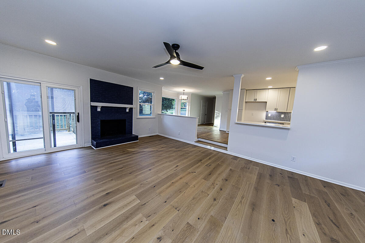1208 Lorimer Road Raleigh, NC 27606 - Photo 8 of 37 an empty room with wooden floor fireplace and a kitchen view