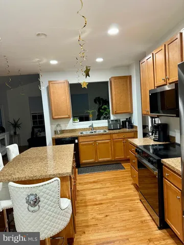 a kitchen with stainless steel appliances kitchen island granite countertop a stove a sink dishwasher a dining table and chairs with wooden floor