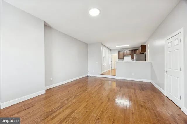 a view of empty room with wooden floor and kitchen