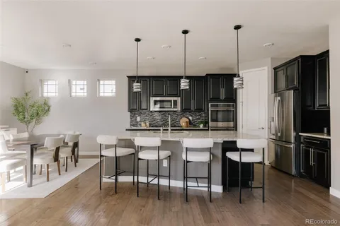 a kitchen with stainless steel appliances granite countertop a stove top oven a refrigerator a dining table and chairs with wooden floor