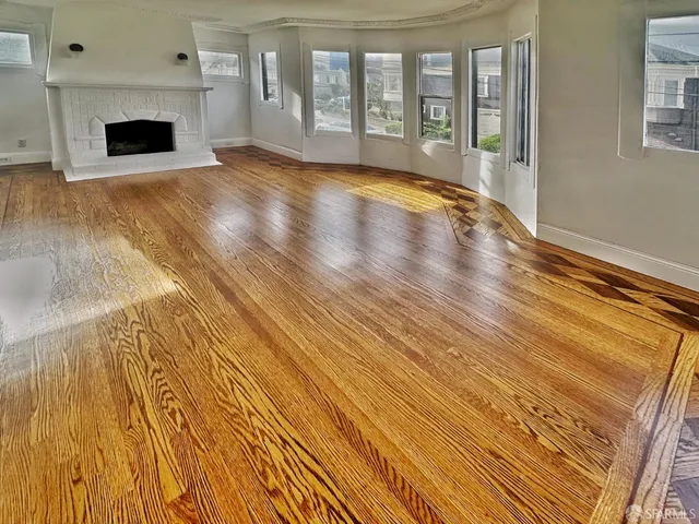 a view of an empty room with wooden floor and a fireplace