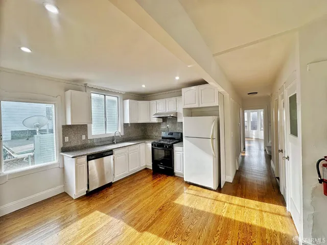 a large kitchen with a refrigerator a sink dishwasher a stove and white cabinets with wooden floor