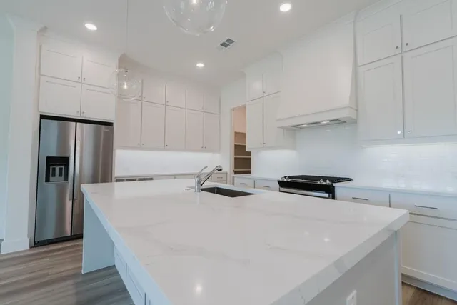 a kitchen with stainless steel appliances a stove a refrigerator a sink and white cabinets