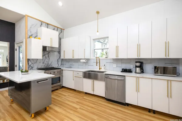 a kitchen with stainless steel appliances granite countertop a stove a sink dishwasher and white cabinets with wooden floor