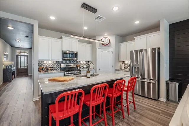 a kitchen with stainless steel appliances granite countertop a refrigerator a stove top oven a sink dishwasher and white cabinets with wooden floor