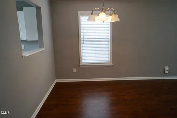an empty room with wooden floor chandelier and window