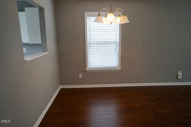 an empty room with wooden floor chandelier and window