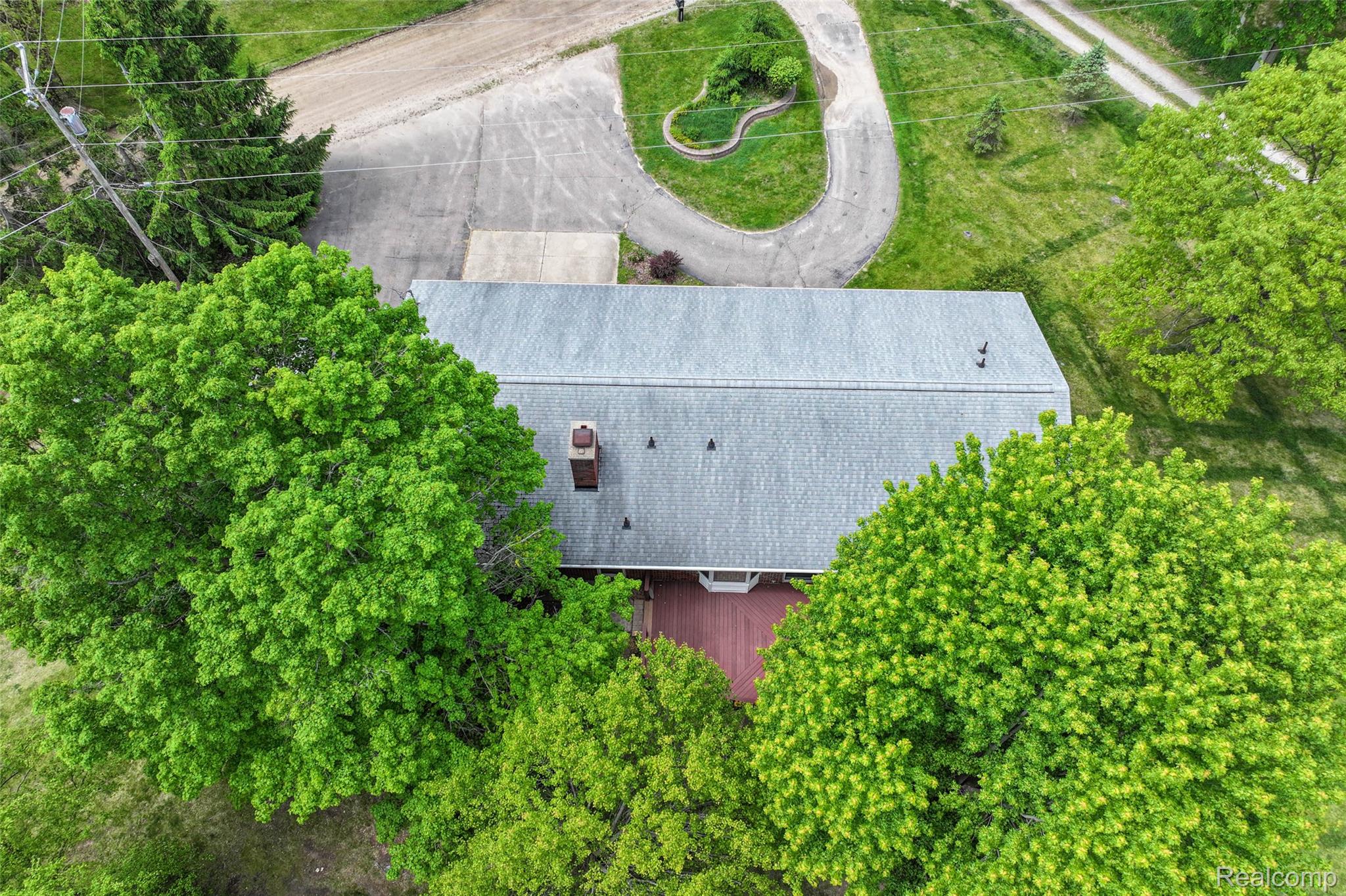 422 East Road Holly, MI 48442 - Photo 45 of 51 Gray shingle roof structure featuring a red-toned deck, multiple mature trees, and a paved driveway