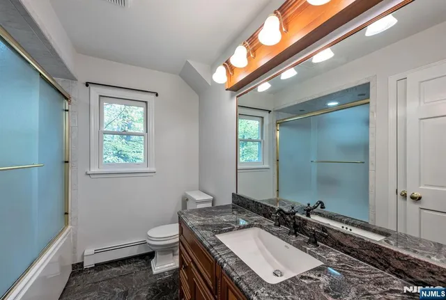 a bathroom with a granite countertop sink a toilet a mirror and a window