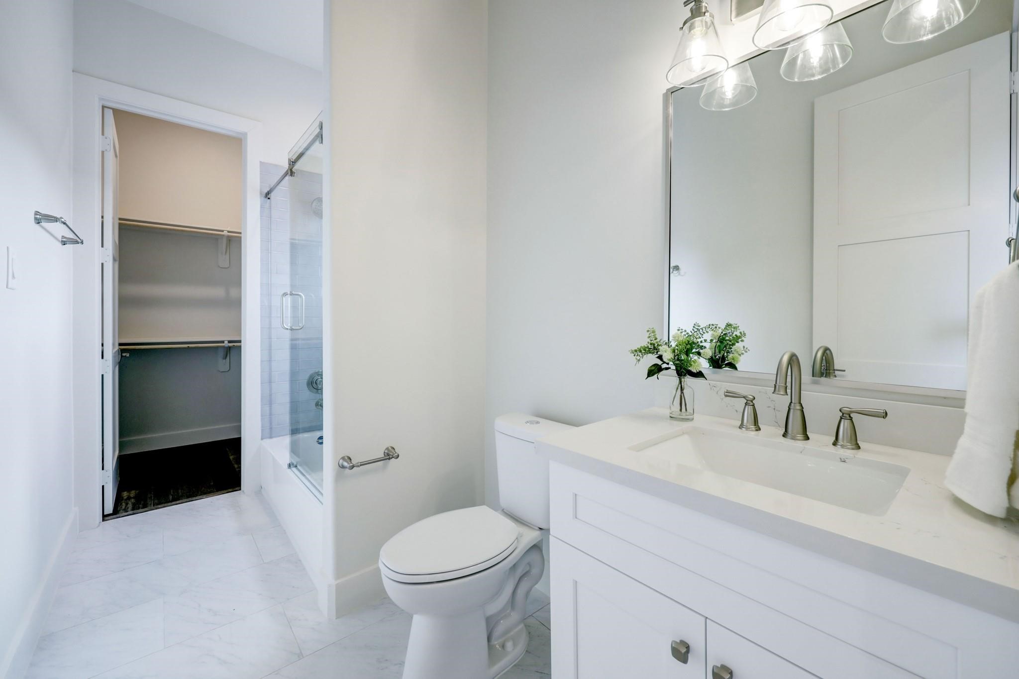 3827 Arlington Street Houston, TX 77018 - Photo 30 of 39 This bathroom features a sleek vanity with a large mirror, elegant lighting, and a glass-enclosed shower. It opens into a spacious walk-in closet, offering convenience and ample storage.