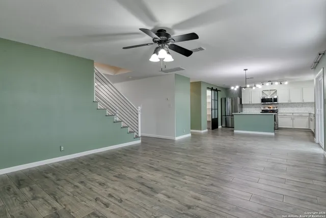 a view of an empty room with wooden floor and a ceiling fan