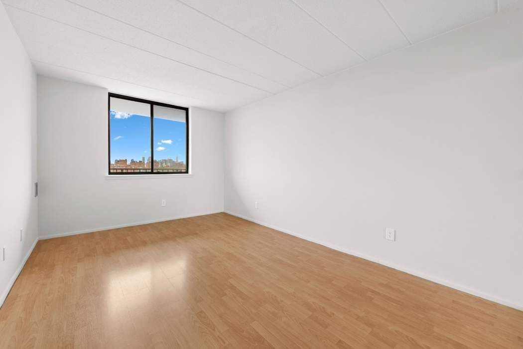 23-22 30th Road, Unit 10H Queens, NY 11102 - Photo 5 of 16 a view of an empty room with wooden floor and a window