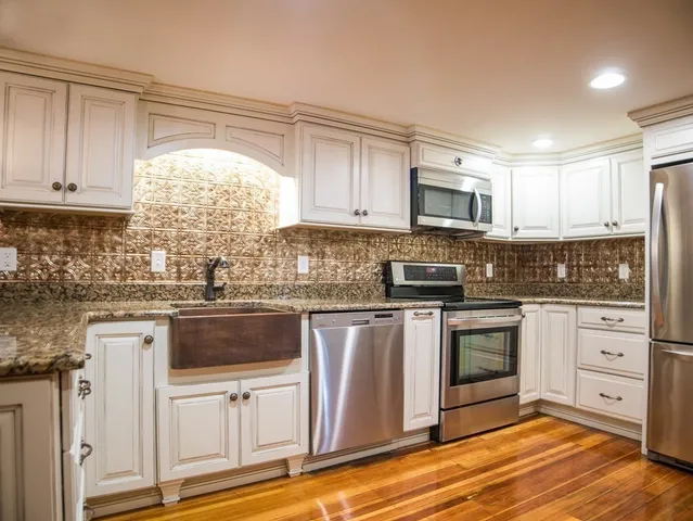 a kitchen with granite countertop white cabinets stainless steel appliances a sink and a window