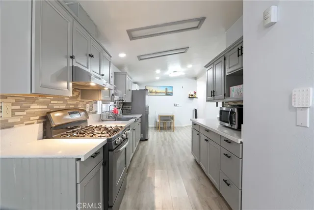 a kitchen with stainless steel appliances granite countertop a stove top oven a sink dishwasher and a refrigerator with wooden floor