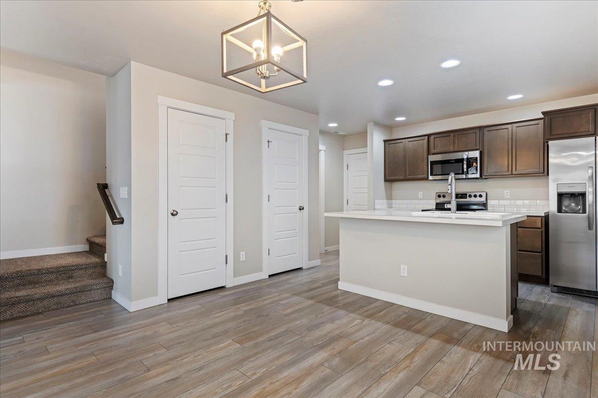2501 East Goldstone Street Meridian, ID 83642 - Photo 7 of 26 Kitchen with stainless steel appliances, dark wood finish cabinetry, a center island with sink, suspended lighting, and light wood-style floors