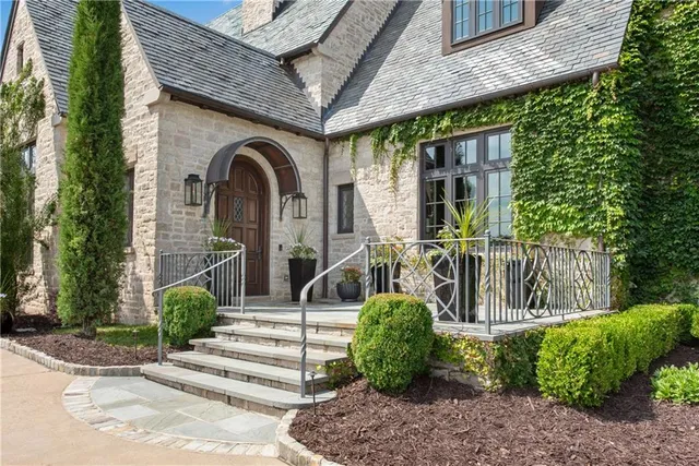 a view of a brick house with a yard plants and large tree