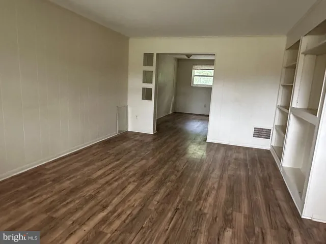 a view of empty room with wooden floor and kitchen