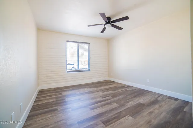 an empty room with wooden floor fan and windows