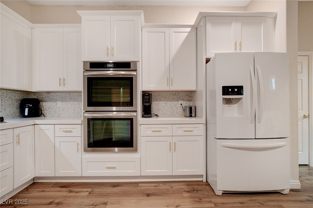 10720 Elm Ridge Avenue Las Vegas, NV 89144 - Photo 10 of 67 Kitchen featuring white fridge with ice dispenser, stainless steel double oven, white cabinetry, and light wood finished floors