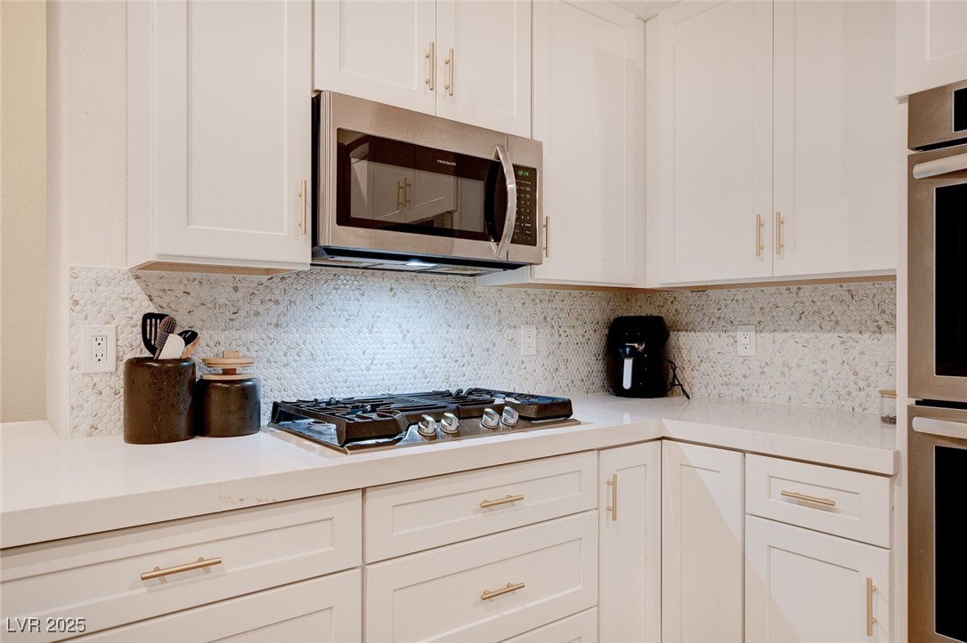 10720 Elm Ridge Avenue Las Vegas, NV 89144 - Photo 11 of 67 Kitchen featuring appliances with stainless steel finishes, white cabinetry, decorative backsplash, and light stone counters